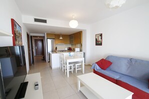A modern living room with a red sofa, a white coffee table, and a TV. There's a kitchen area with wooden cabinets and a dining table. - Panoramic 24 by Parc Mont-roig Apartment (Miami Playa)