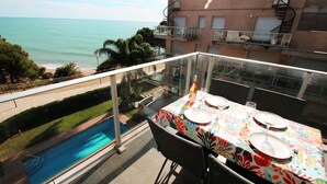 En balkon med spiseplads, der giver udsigt over en swimmingpool og havet.