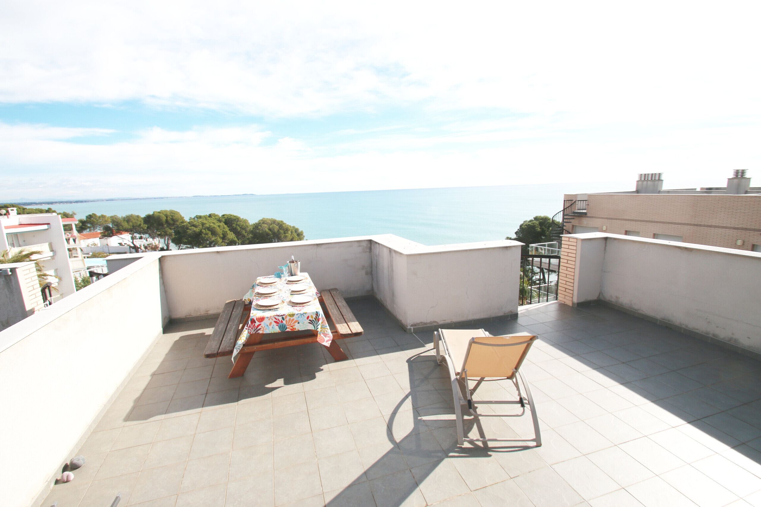 Terraço no telhado com uma mesa posta para refeições, uma cadeira e vista para o mar.