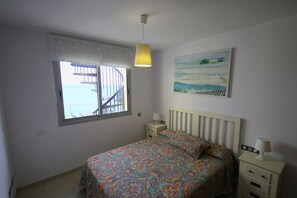 Ein Schlafzimmer mit Bett, Fenster mit Blick, einem Bild an der Wand und einem Nachttisch mit Lampe.