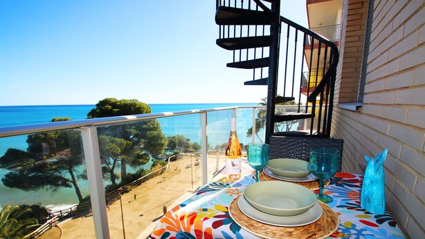 Un balcón con una mesa lista para comer, con vista a una playa y al mar.
