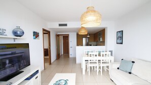 Una sala de estar moderna con televisor de pantalla plana, muebles blancos y una zona de comedor con mesa y sillas blancas.
