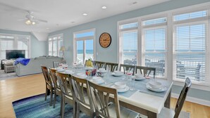 A dining area with a table set for six, a ceiling fan, and a view of the ocean through large windows. - Oceanfront | Pet Friendly | Elevator | Hot Tub | Pool Access (North Topsail Beach)