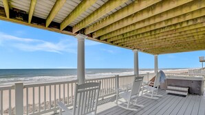 A wooden deck with white rocking chairs, a barbecue area, and a view of the ocean. - Oceanfront | Pet Friendly | Elevator | Hot Tub | Pool Access (North Topsail Beach)