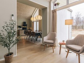 Una sala de estar moderna con comedor, una cocina al fondo y un ventanal con cortinas.
