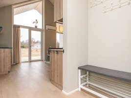 Un interior moderno con piso de madera, un banco con espacio de almacenamiento y vistas a través de un ventanal.