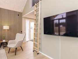 A modern living room with a flat-screen TV mounted on the wall, a wooden slatted wall design, a checkered chair, and a small table with a lamp.