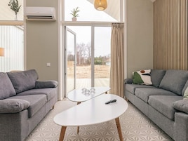 Una sala de estar con dos sofás grises, una mesa de centro blanca y un ventanal corredizo que da a un espacio exterior.