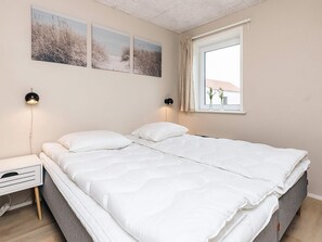 Egy hálószoba, amelyben található egy ágy, éjjeliszekrények, egy függönnyel ellátott ablak és a falra szerelt műalkotások.