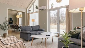 Una sala de estar moderna con un sofá gris, un sillón escocés, una mesa de centro redonda y una planta en maceta.