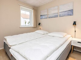 Quarto com cama, mesa de cabeceira, abajur, janela com cortinas e obras de arte nas paredes.