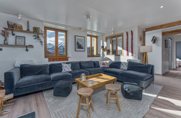 A modern living room with a dark grey sectional sofa, wooden coffee table, and two wooden stools.