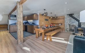 A modern kitchen with wooden cabinetry, a dining area with a wooden table and benches, and a stone wall.