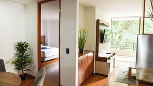 A modern living room with a wooden floor, a dining table, a sofa, a TV, and a large window with a view of greenery. - Exclusive apartment close to Laureles and Provenza (Medellín)