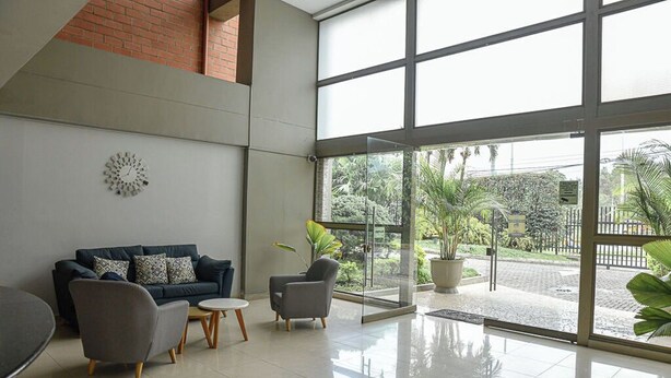 A modern lobby with a glass door leading to an outdoor area, a dark-colored sofa with patterned cushions, and a small round table. - Exclusive apartment close to Laureles and Provenza (Medellín)