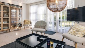 A modern living room with a glass cabinet, two chairs, a coffee table, and a large hanging light fixture. - 6 Person Holiday Home in Dannemare (Dannemare)