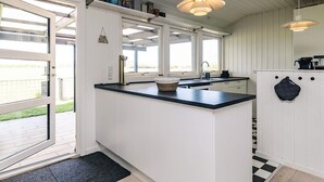 A kitchen with white cabinetry, a black countertop, a hanging light fixture, and a view through the window. - 6 Person Holiday Home in Dannemare (Dannemare)