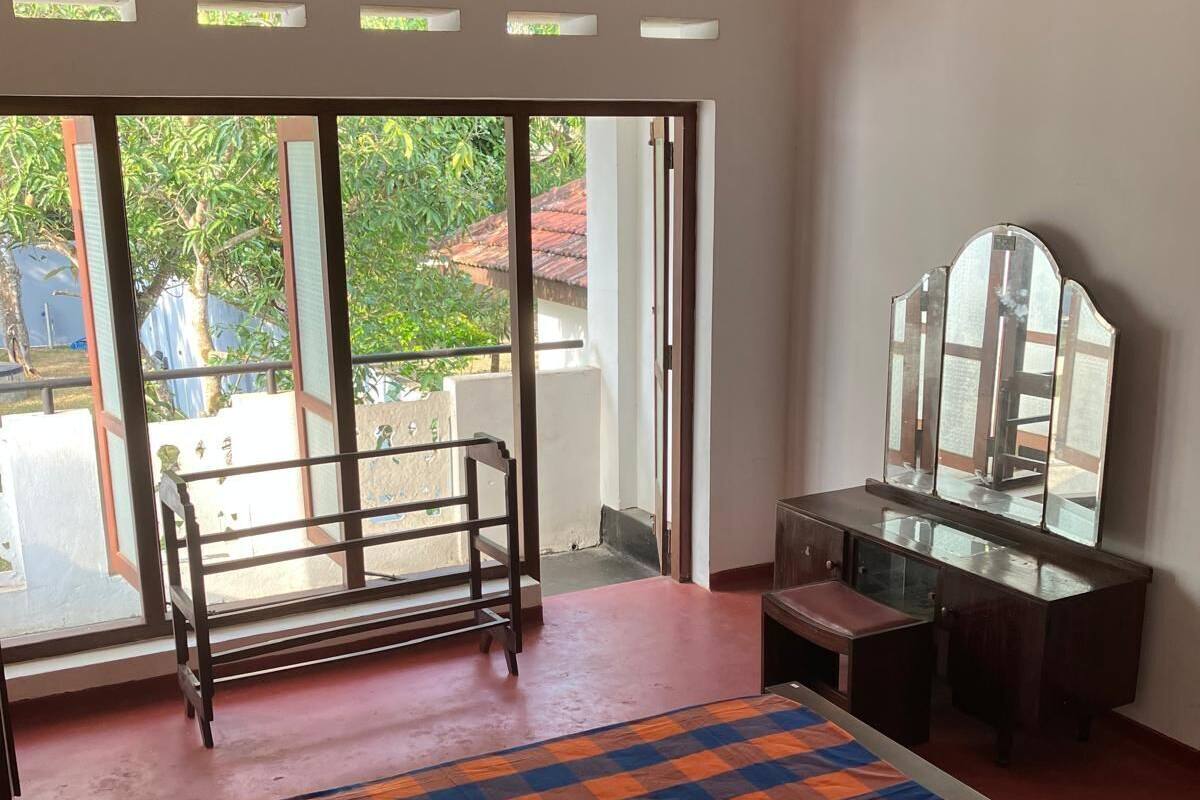 A room with a bed, a desk, and a large window with a view of greenery outside.
