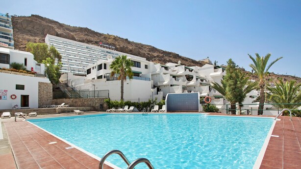 A swimming pool with a view of a hotel and a mountain in the background. - Vacation Apartment 'Dúplex Guayana 23 En Puerto Rico' with Mountain View, Shared Pool and Wi-Fi (Mogán)
