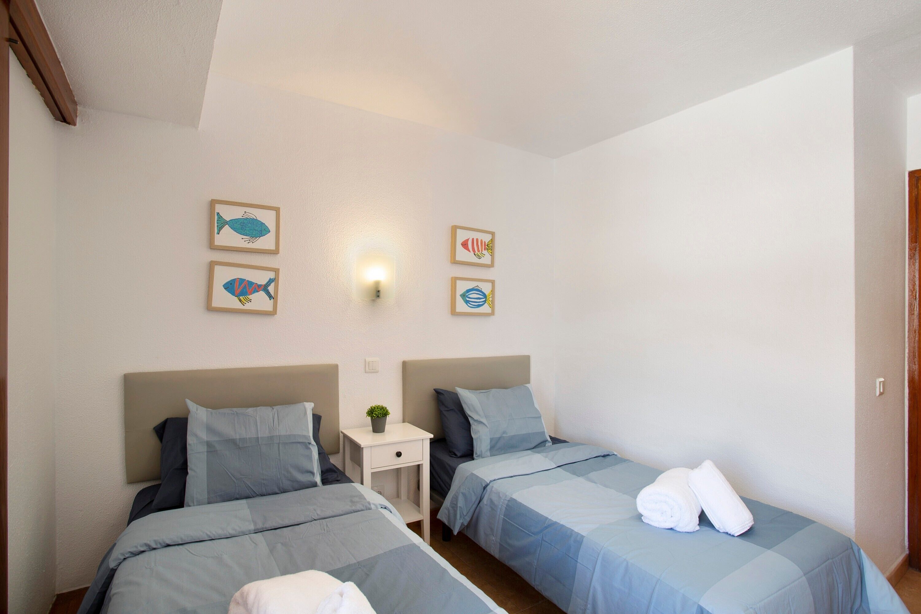 Une chambre d’hôtel avec deux lits, une table de chevet ornée d’une plante et des œuvres d’art murales représentant des poissons.