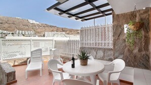 A terrace with a round table, white chairs, a bottle of wine, and a potted plant. - Vacation Apartment 'Dúplex Guayana 23 En Puerto Rico' with Mountain View, Shared Pool and Wi-Fi (Mogán)