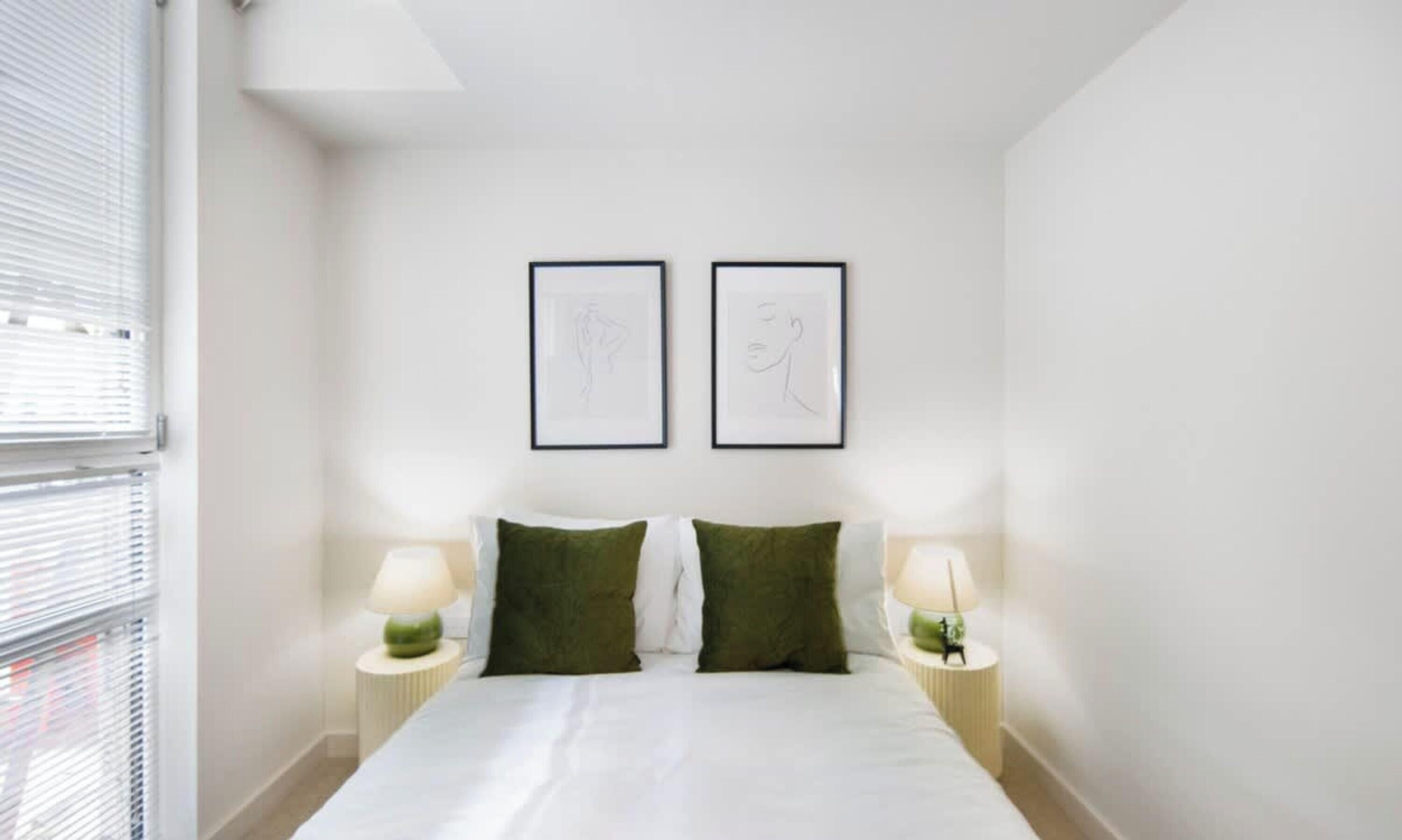Una camera da letto con un letto, due cuscini, due comodini con lampade e due opere d'arte appese alla parete.