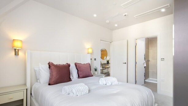 A modern hotel room with a large bed, two bedside lamps, a mirror, and a door leading to a bathroom. - 5 Mins Walk to Battersea Park Battersea Retreat (London)