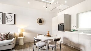 A modern kitchen with white cabinetry, a round dining table with four chairs, a small side table with a lamp, and a decorative vase. - 5 Mins Walk to Battersea Park Battersea Retreat (London)
