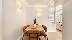 Un comedor con una mesa de madera y seis sillas, un jarrón con plantas secas y dos luces fijadas a la pared.