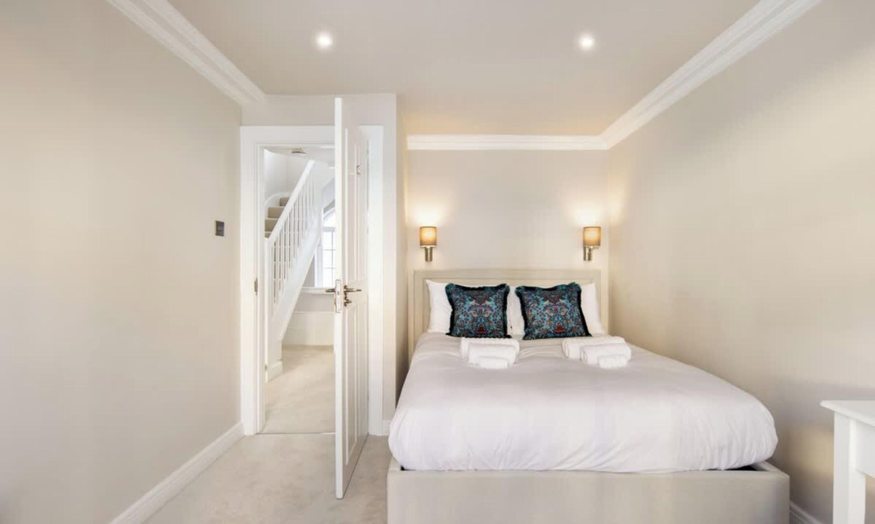 A bedroom with a large bed, two decorative pillows, a nightstand, and a wall-mounted light fixture.