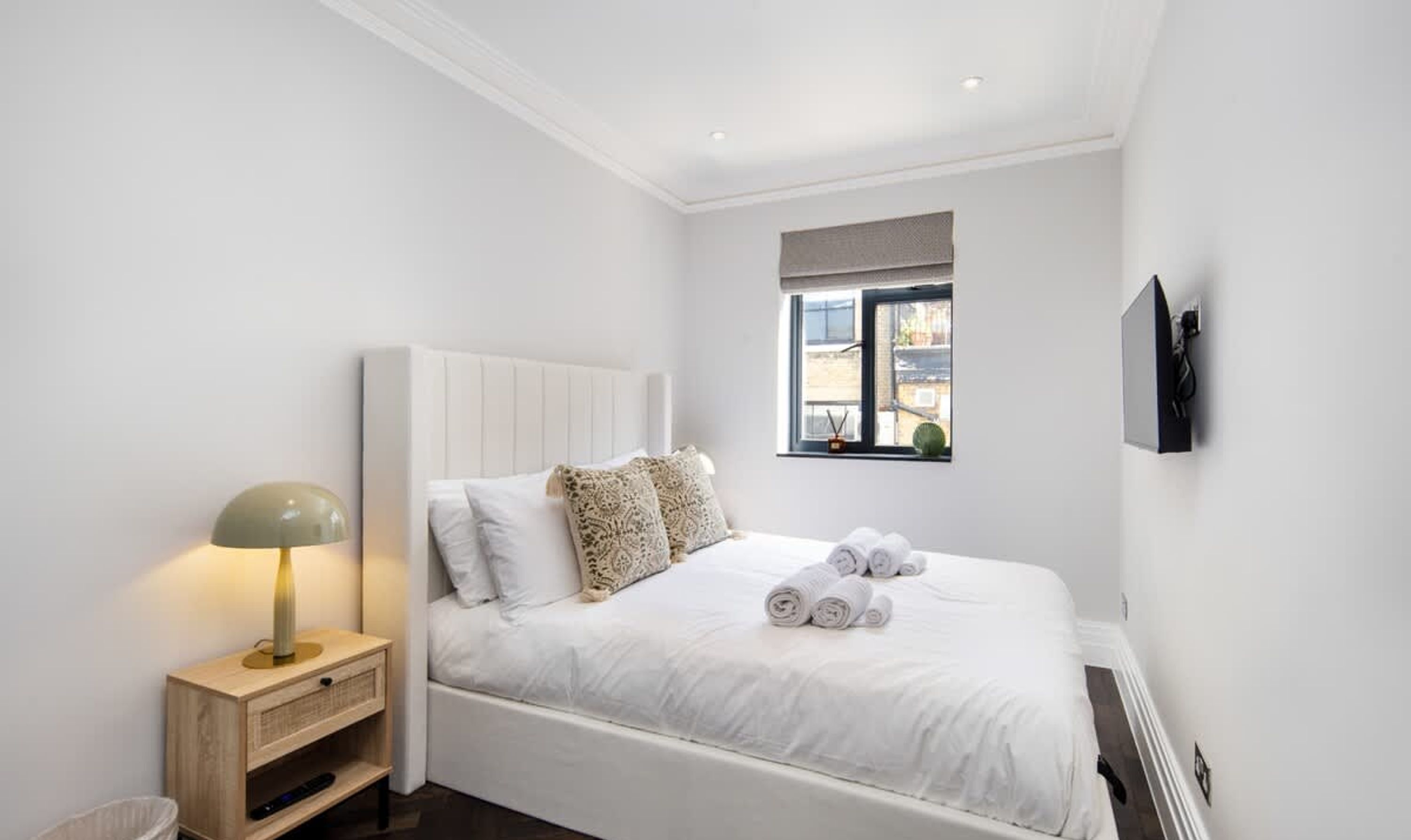 Een minimalistisch ingerichte slaapkamer met een bed, bedlamp en een raam met uitzicht.