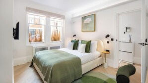Un dormitorio con cama, lámparas de noche, un radiador, una ventana y una puerta.