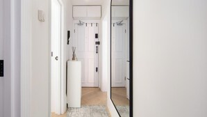 Un pasillo con puertas blancas, un pilar blanco y un espejo que refleja el pasillo.