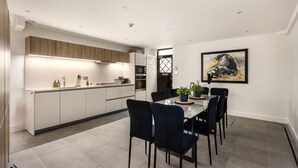 Une cuisine moderne avec des meubles blancs, un four encastré et un coin repas comprenant une table en verre et des chaises noires.