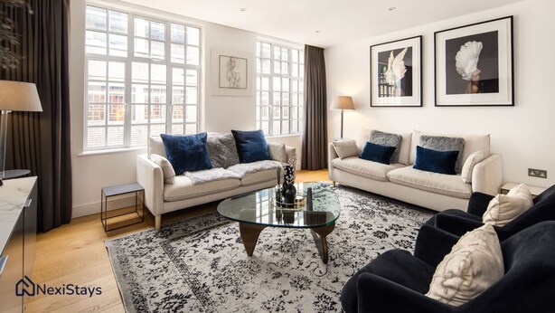 Un salon moderne avec deux canapés blancs, une table basse en verre et un tapis à motifs.