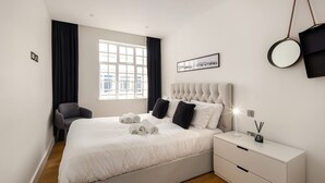 Une chambre moderne avec un grand lit, une table de chevet, une chaise, une fenêtre avec des rideaux, un tableau encadré et un miroir.