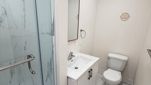 Casa de banho com chuveiro em cabine de vidro, lavatório branco com espelho em cima e sanita.