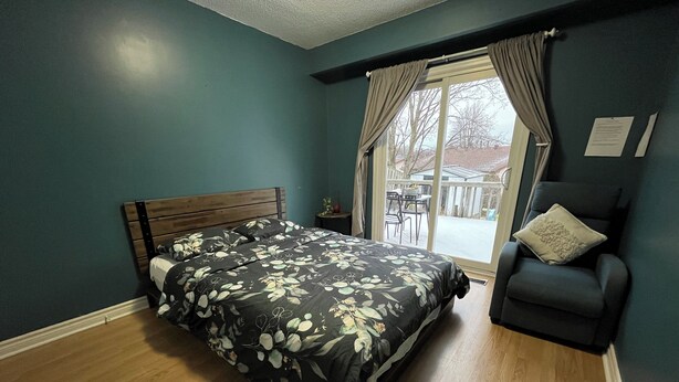 Quarto com cama de madeira, parede azul escuro e vista do exterior por uma porta de correr de vidro.