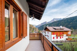 A balcony with a wooden railing, a view of a mountain, and a building with red shutters. - Apartment 'Sasedel' with Mountain View and Shared Garden (Caviola)