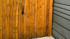 Une clôture en bois portant le numéro 3308, une maison avec un revêtement extérieur gris et un petit luminaire fixé au mur.