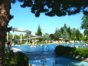 Una piscina con tobogán de agua, rodeada de árboles y sillas de descanso.