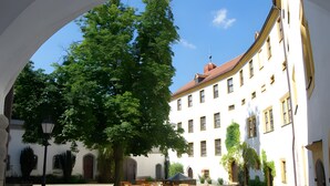 Une cour avec un grand arbre, un bâtiment doté de nombreuses fenêtres et des sièges installés à l’extérieur.