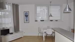 Une cuisine moderne avec un coin repas, des meubles blancs et une fenêtre équipée de stores.