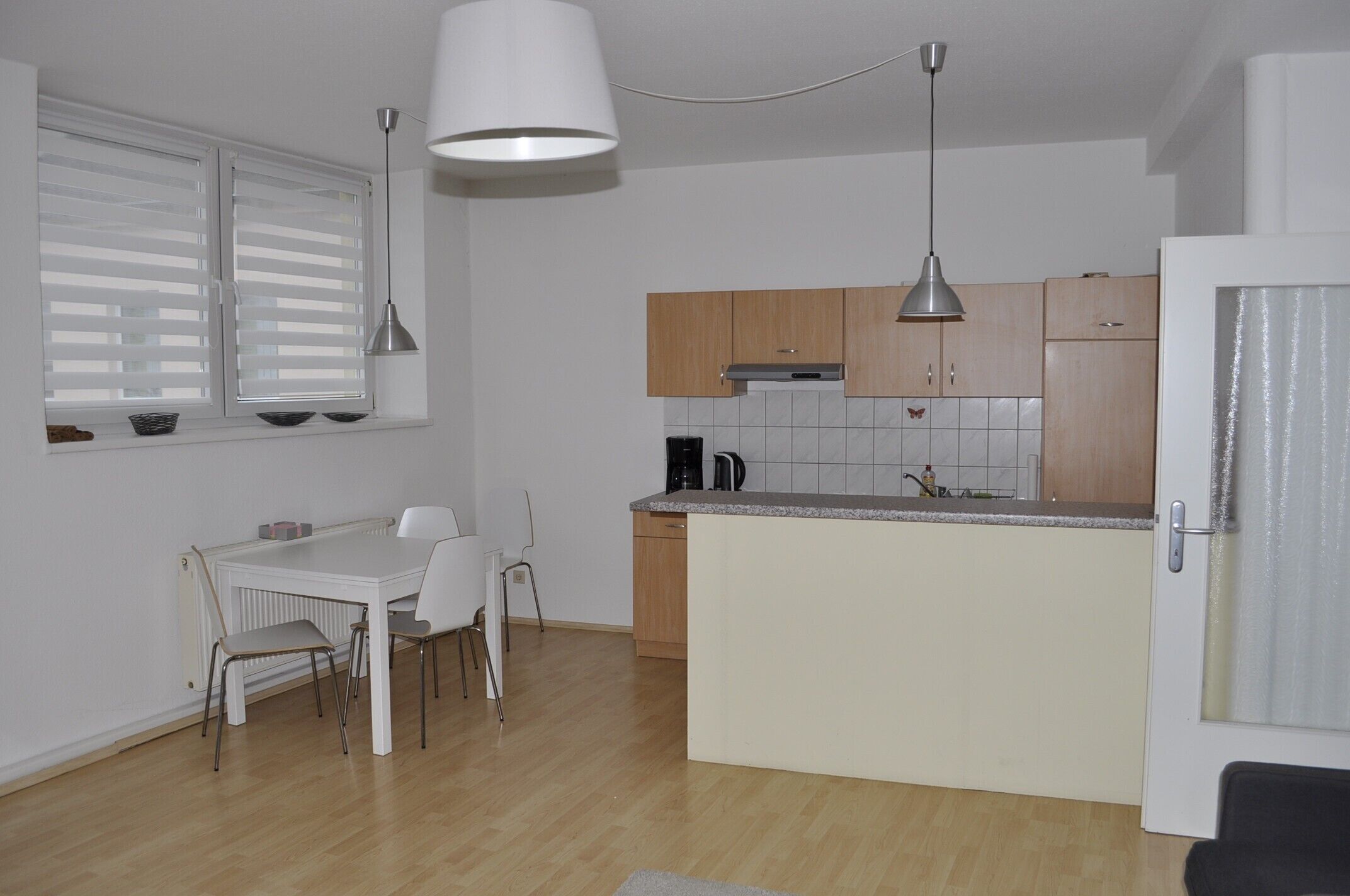Una cocina compacta con comedor, armarios de madera y encimera blanca.