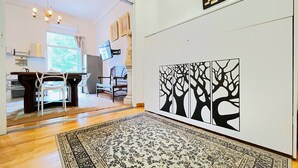 Une pièce dotée d’un plancher en bois, d’un tapis à motifs, d’un coin repas avec des chaises et une table, et d’un mur orné d’une œuvre d’art représentant un arbre en noir et blanc.