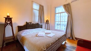 Une chambre à coucher avec un grand lit, deux tables de chevet, une commode et une fenêtre avec des rideaux.