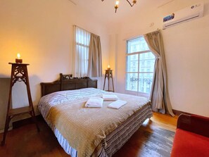 Ein Schlafzimmer mit einem großen Bett, zwei Nachttischen, einer Kommode und einem Fenster mit Vorhängen.