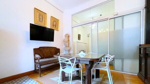 Un espace repas comprenant une table en verre, des chaises blanches, un banc en bois et un canapé.