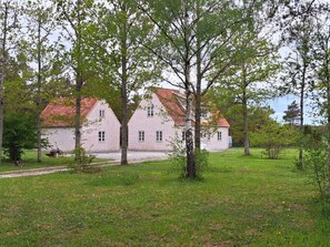 A traditional two-story house with a red-tiled roof, surrounded by a grassy area with trees.