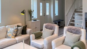 Uma sala de estar com sofá, poltronas, mesa de centro, abajur e escada.